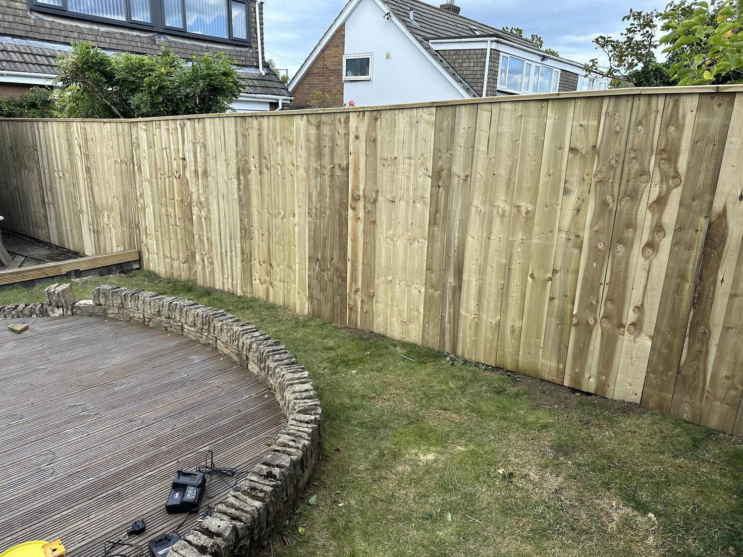 A new boarded fence beside a circular deck and a low stone edge