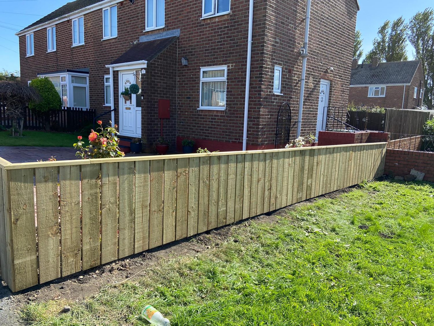 A long new timber fence along a lawn in front of a semi-detached house