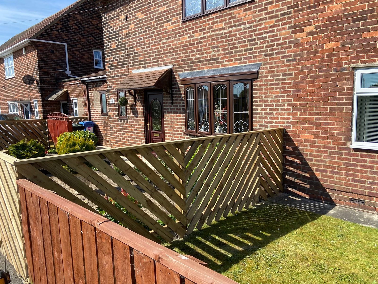 A herringbone lattice fence beside a house, with a darker fence below it