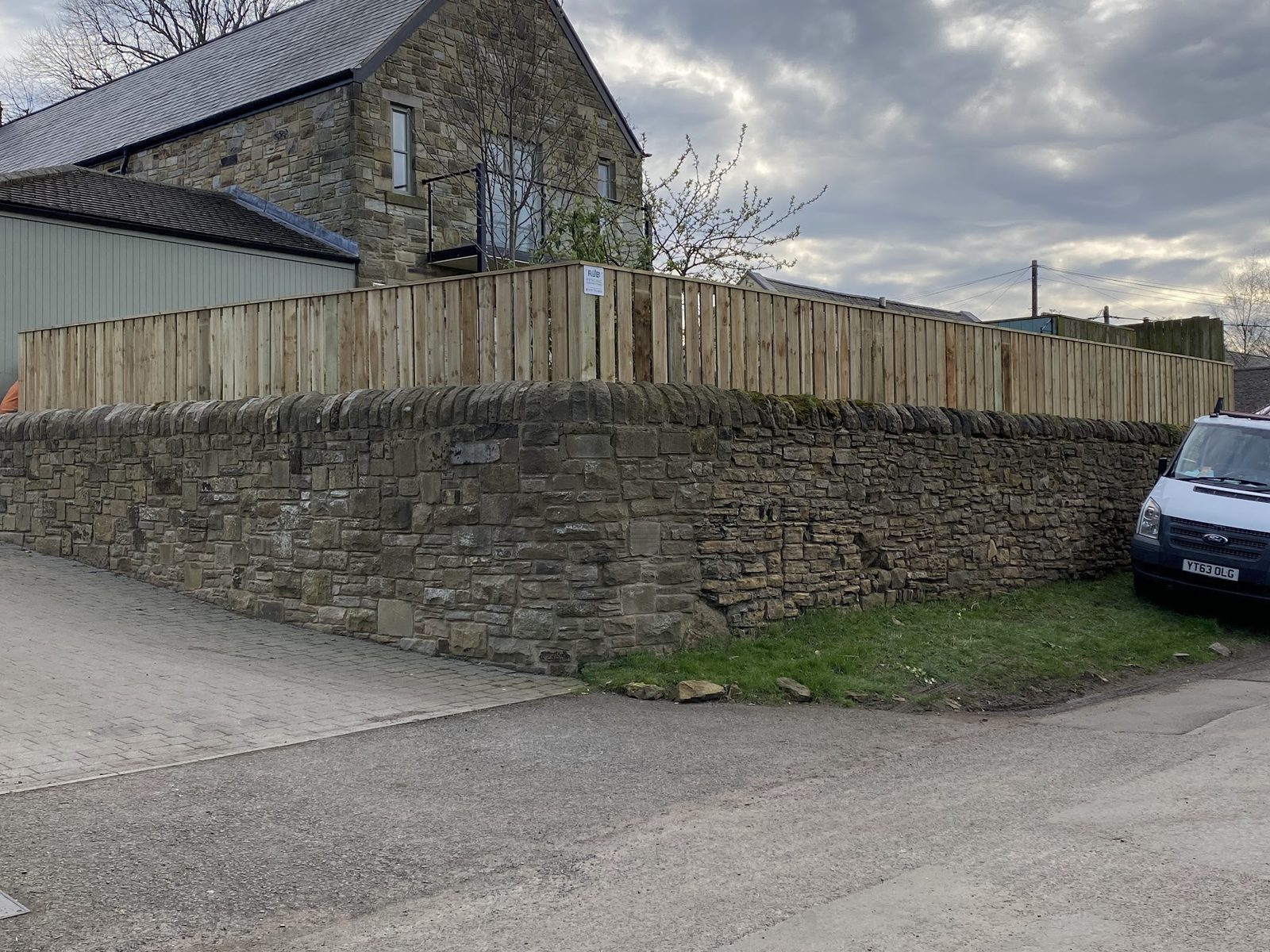 A new timber fence above an old stone wall on a village corner