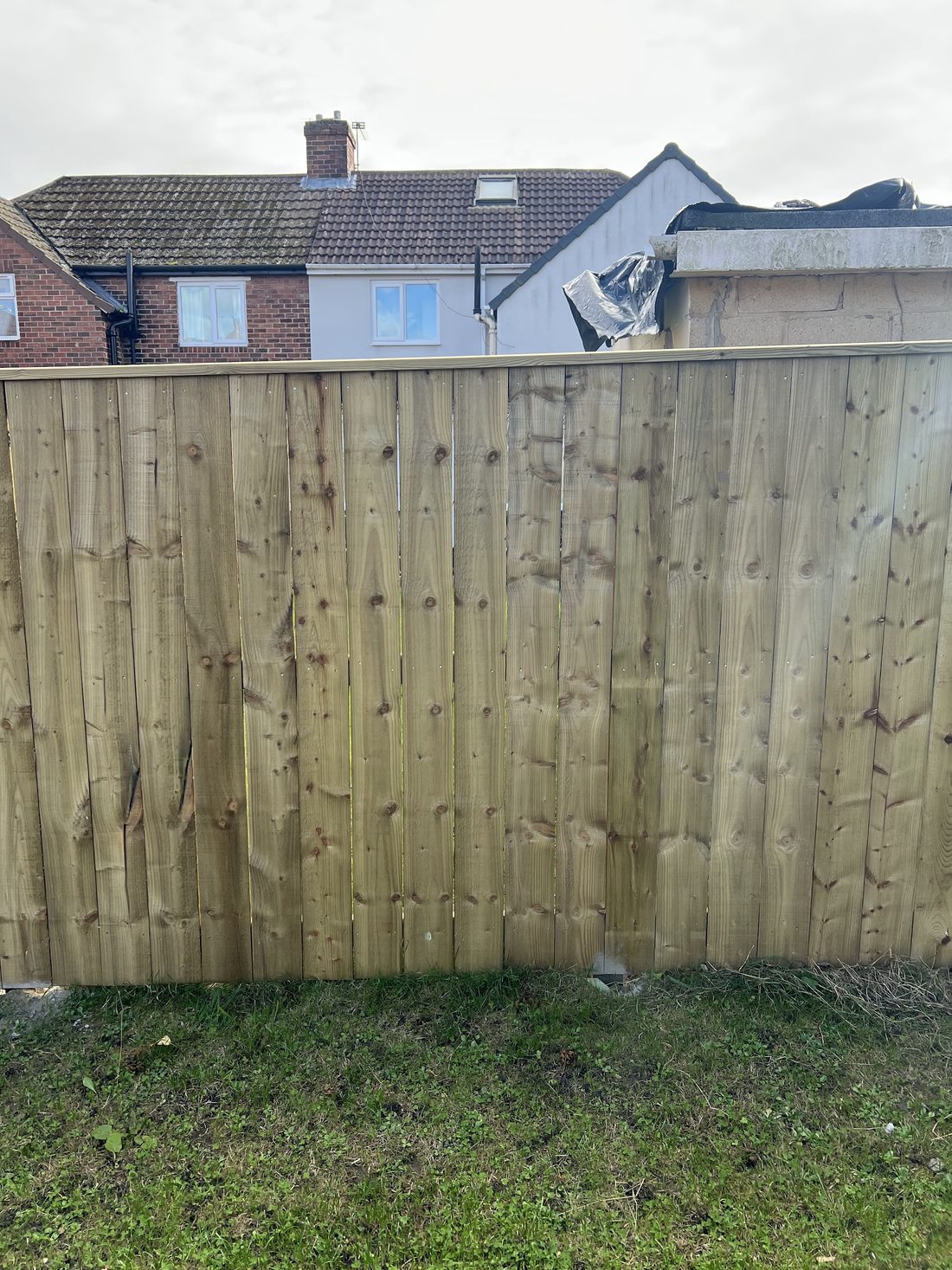 A tall new boarded fence against a grey sky